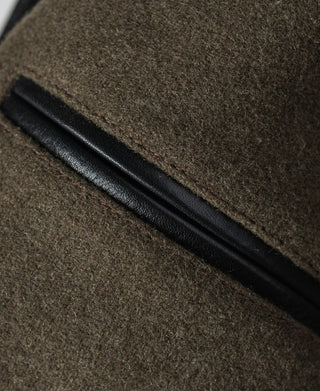 Coat detail with a black leather welt over textured brown wool fabric