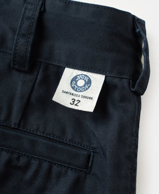 Navy cotton twill trousers with brand tag on waistband and front pocket opening.