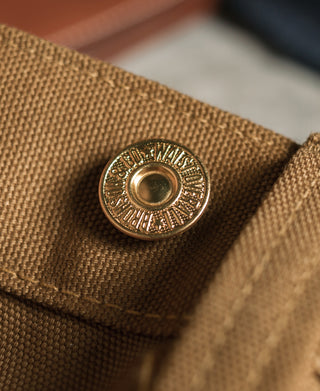 Round metal button with engraved detail on brown canvas pants
