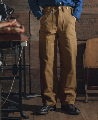 Brown double-knee canvas pants with straight legs, front closure, and multiple utility pockets.