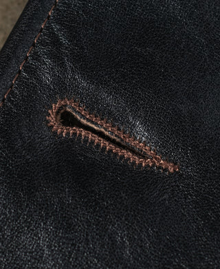 Close-up of a brown-stitched buttonhole on black leather