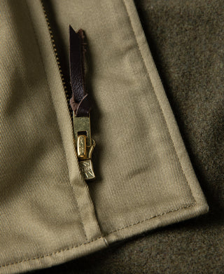 Yellow-green jacket hem corner with brass zipper and pocket seam detail.