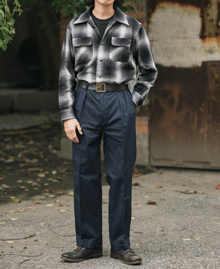 Navy cotton twill double-pleat trousers on model, straight leg with belt and front pockets.
